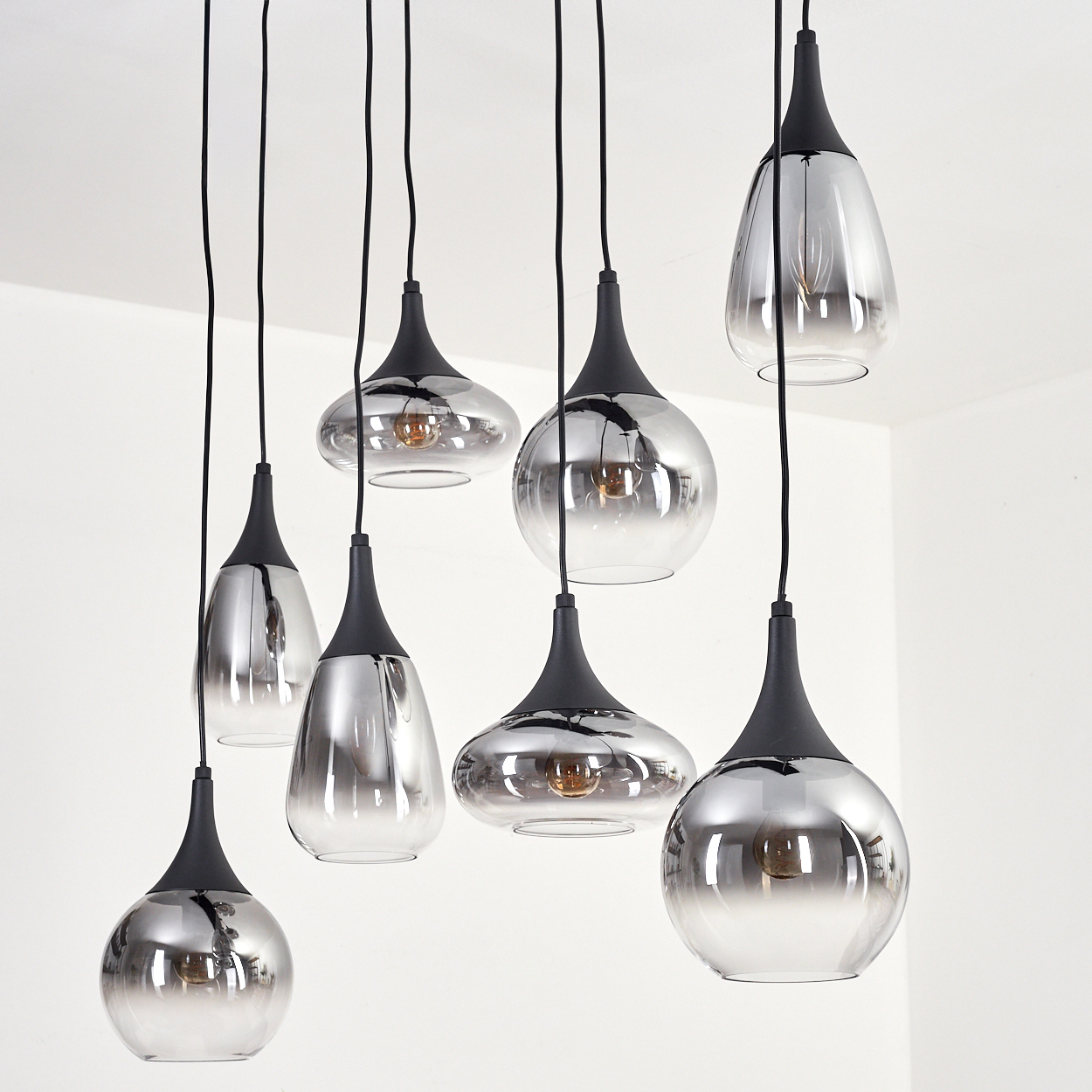 Mehrere moderne Pendelleuchten mit schwarzen Oberteilen und reflektierenden Glasschirmen hängen vor weißem Hintergrund.