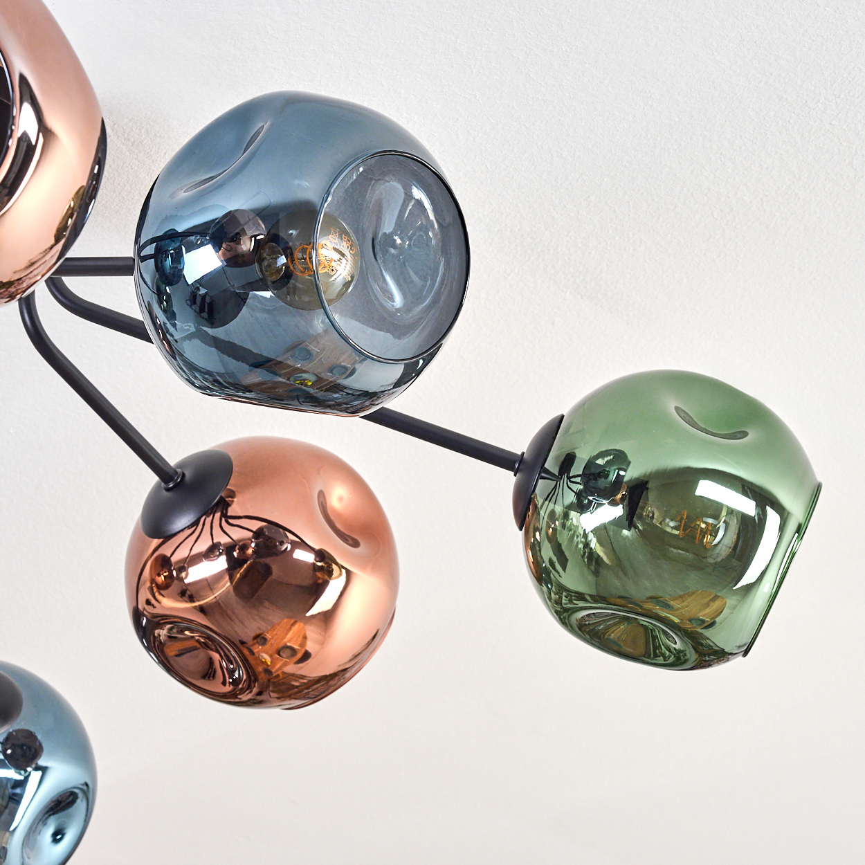Eine moderne Deckenleuchte mit mehreren kugelförmigen Glasschirmen in Blau, Kupfer und Grün, die an schwarzen Metallarmen befestigt sind.
