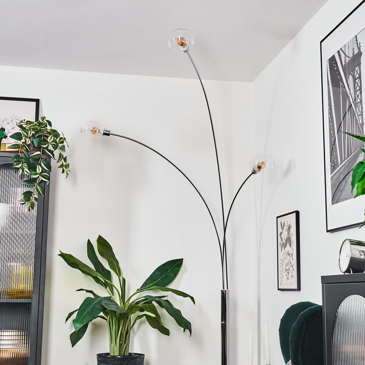 Eine moderne Stehlampe mit drei Glaskugelleuchten. Davor steht eine Topfpflanze. Kunstwerke und Möbel sind ebenfalls zu sehen.