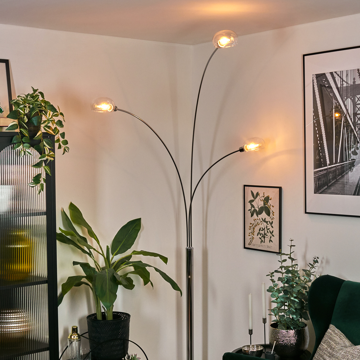 Ein modernes Wohnzimmer mit Stehlampe, Pflanzen, Kunstwerken und einem grünen Sessel, das eine stilvolle Atmosphäre schafft.