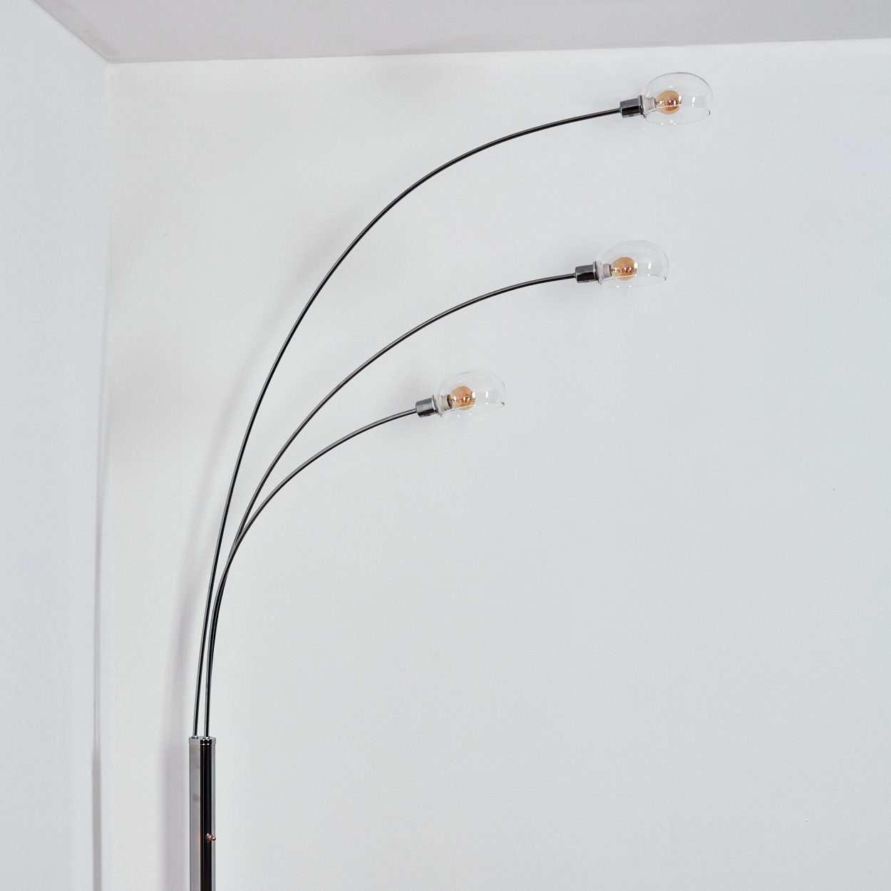 Eine moderne Stehlampe mit drei gebogenen Armen, die jeweils eine klare Glühbirne vor einer weißen Wand halten.