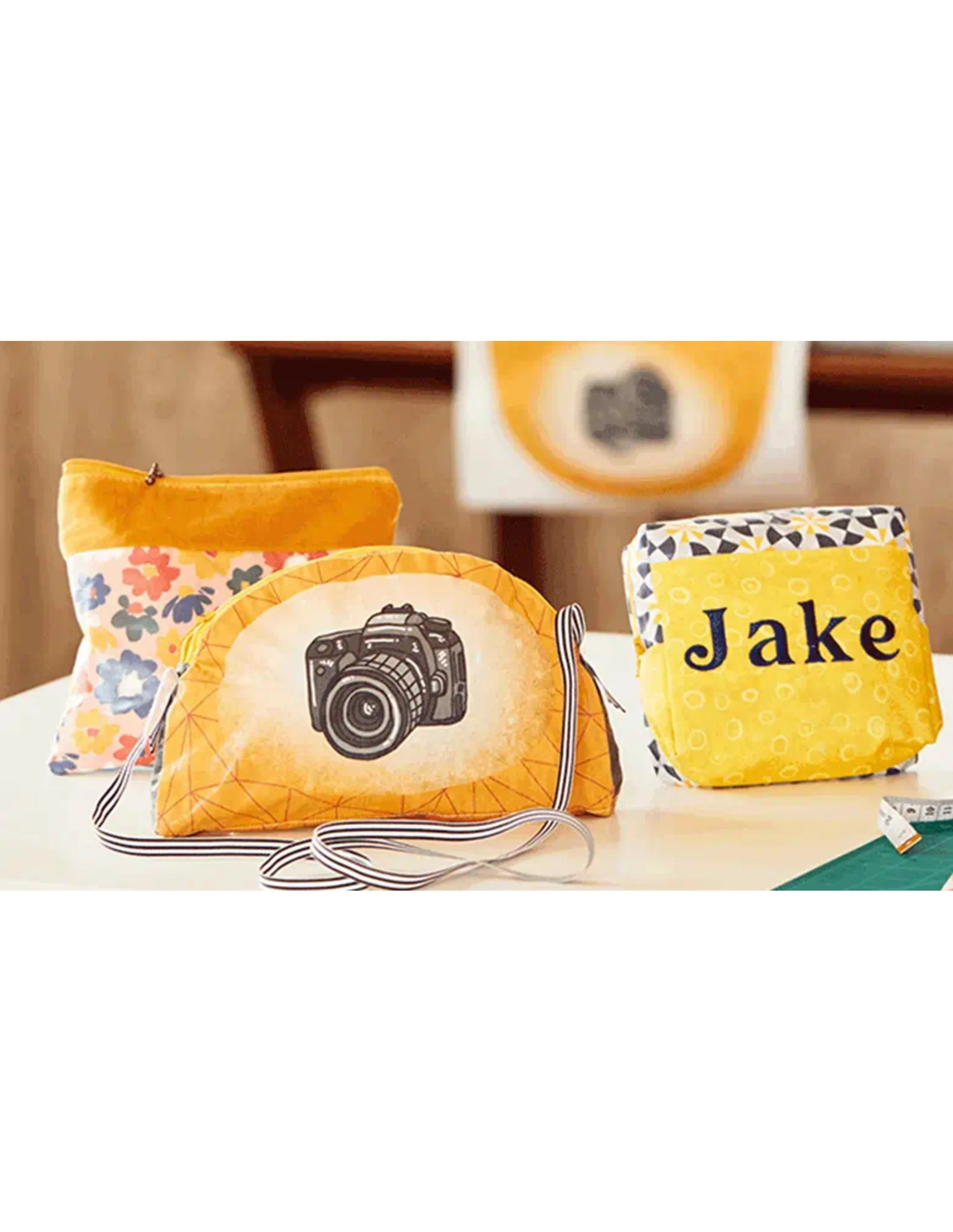 Drie tassen op een wit oppervlak. Eén heeft een camera-afbeelding, een andere bloemen en de laatste zegt 'Jake'.