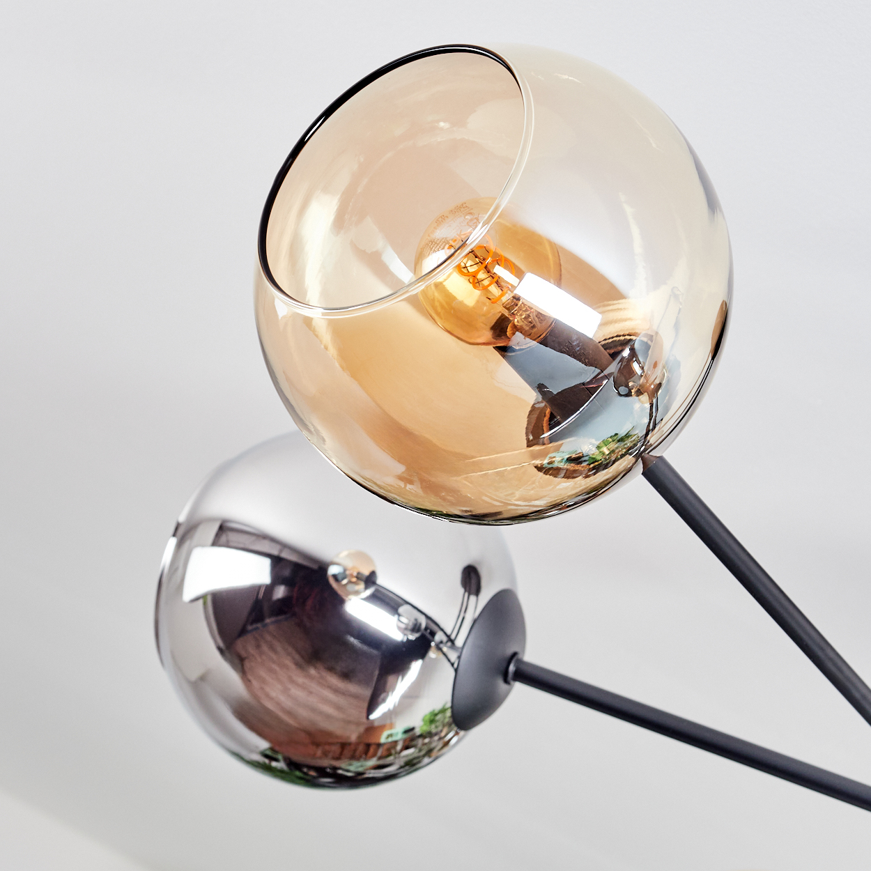 Eine moderne Lampe mit zwei Glaskugeln, eine bernsteinfarben und eine reflektierend. Schwarze Arme erstrecken sich von einem Sockel aus.