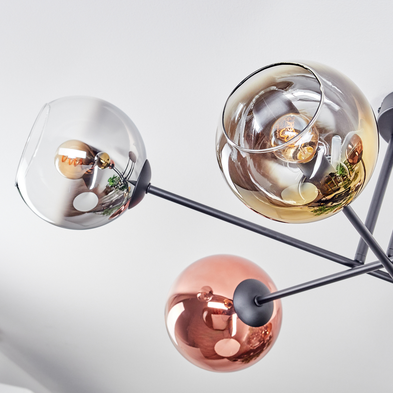 Moderne Deckenleuchte mit kugelförmigen Glasschirmen. Einige sind klar, einige bernsteinfarben, einer kupferfarben. Schwarze Metallarme gehen von der Mitte aus.