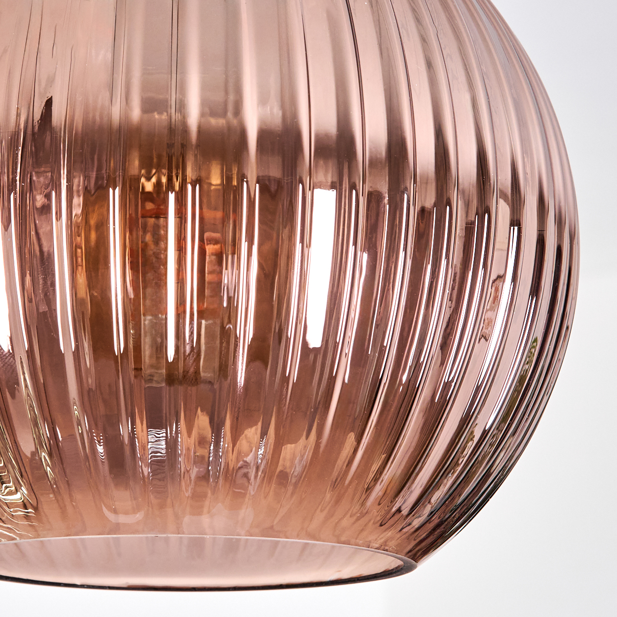 Nahaufnahme einer roségoldenen Glasleuchte. Die geriffelte Oberfläche reflektiert das Licht und zeigt eine interne Glühbirne.