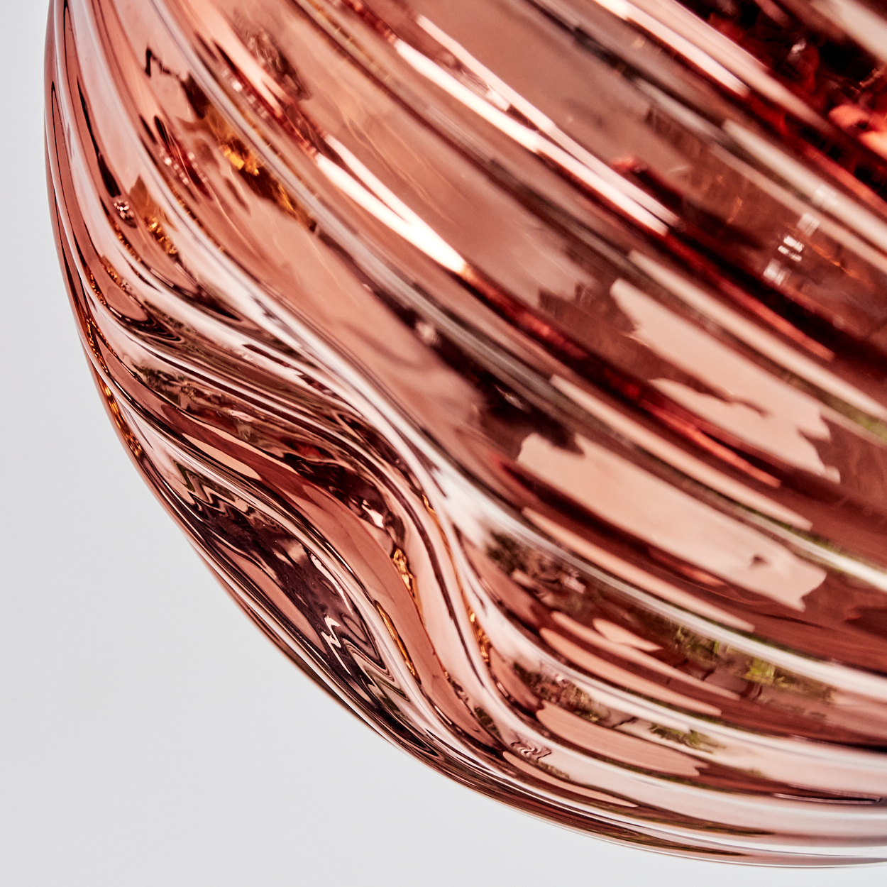 Nahaufnahme einer glänzenden, roségoldenen, wellenförmigen Oberfläche, die Licht reflektiert. Der Hintergrund ist weiß.
