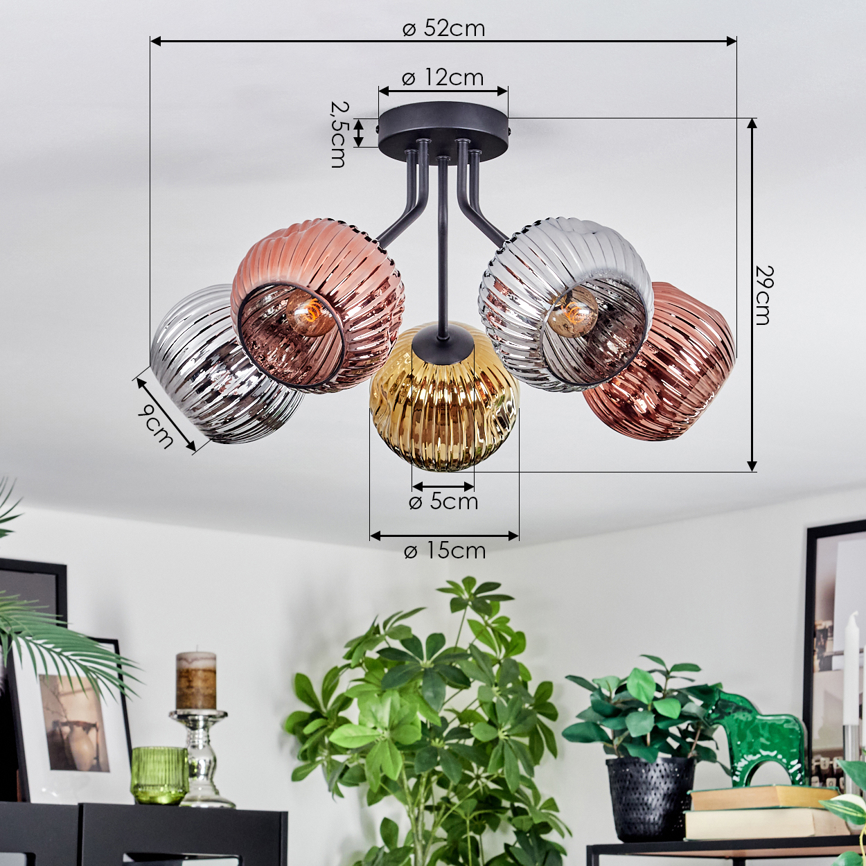 Eine moderne Deckenlampe mit fünf Glaskugeln in Silber-, Kupfer- und Goldfarben. Die Lampe hängt über einem Raum mit Pflanzen und Möbeln.