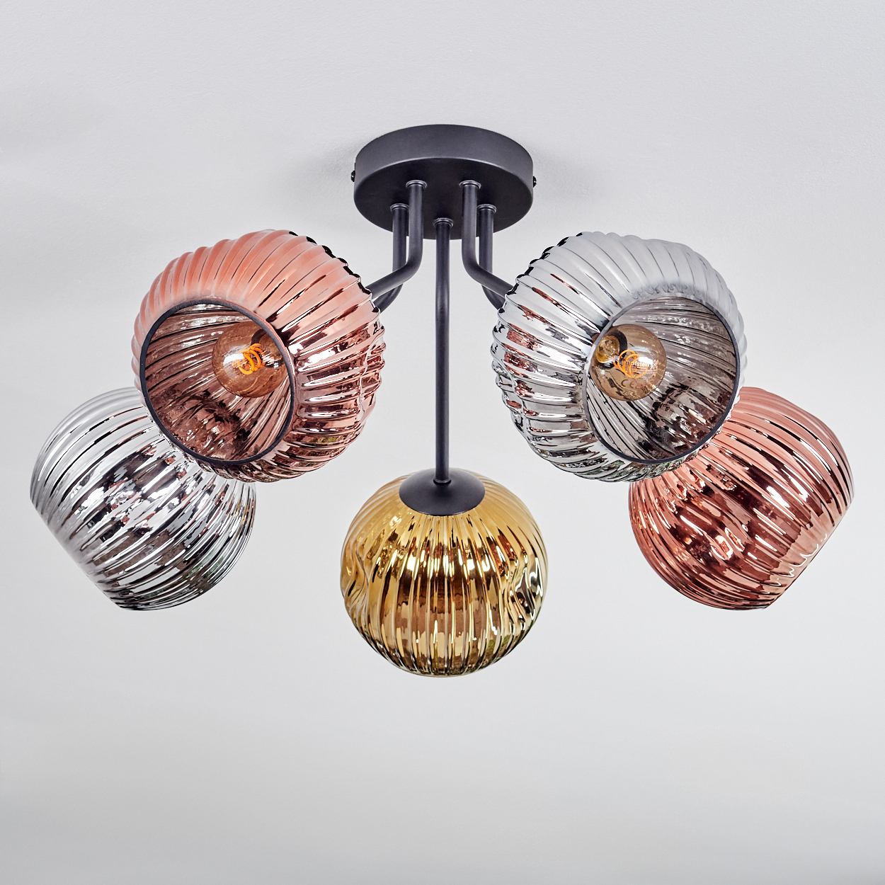 Eine moderne Deckenlampe mit fünf Glasschirmen in Kupfer, Silber und Gold. Die Lampe ist an einem schwarzen Metallrahmen befestigt.