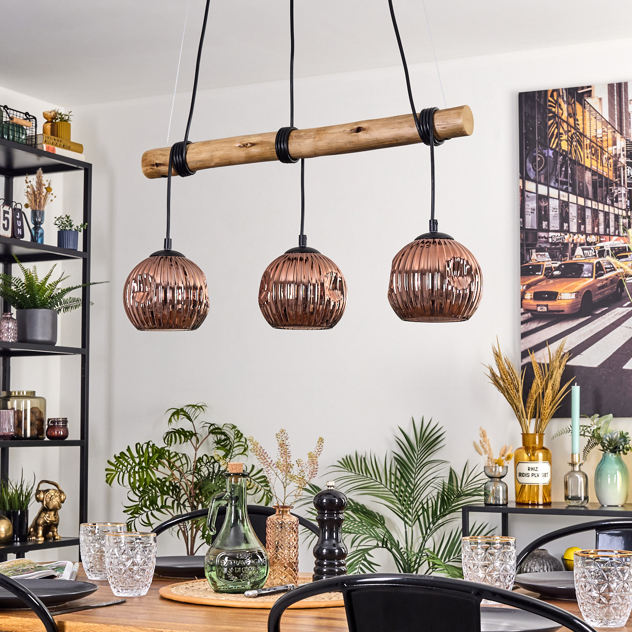 Esszimmer mit Kupfer-Pendelleuchten. Tisch mit Gläsern und Pflanzen. Im Hintergrund ein Stadtbildgemälde.