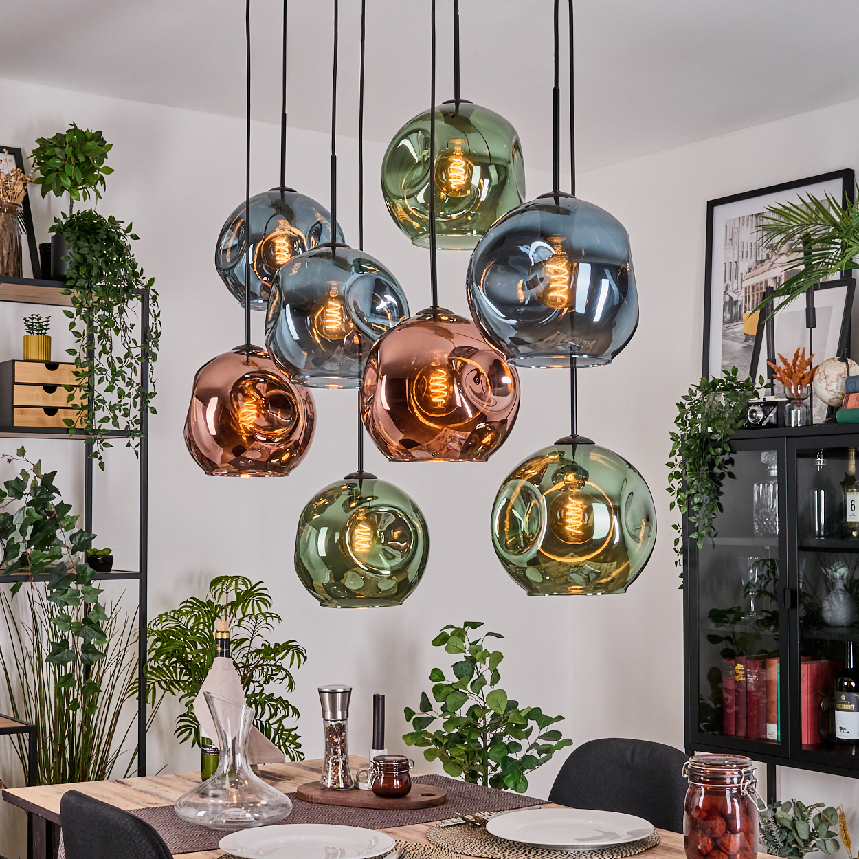 Esszimmer mit Holztisch, Glas-Pendelleuchten und Pflanzen. Gläser mit Essen und Weinflaschen sind sichtbar.