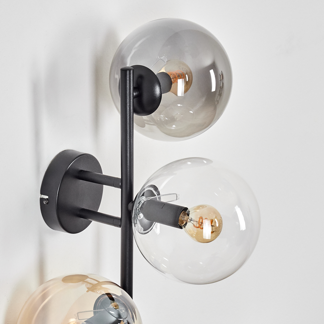 Eine moderne Wandlampe mit drei Glaskugelschirmen. Die Halterung ist schwarz, mit zwei klaren und einer grauen Kugel an einer weißen Wand.