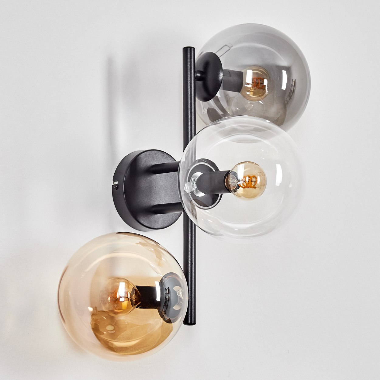 Eine moderne Wandlampe mit drei Glaskugeln. Eine ist grau, eine klar und eine bernsteinfarben, jede mit einer Glühbirne.