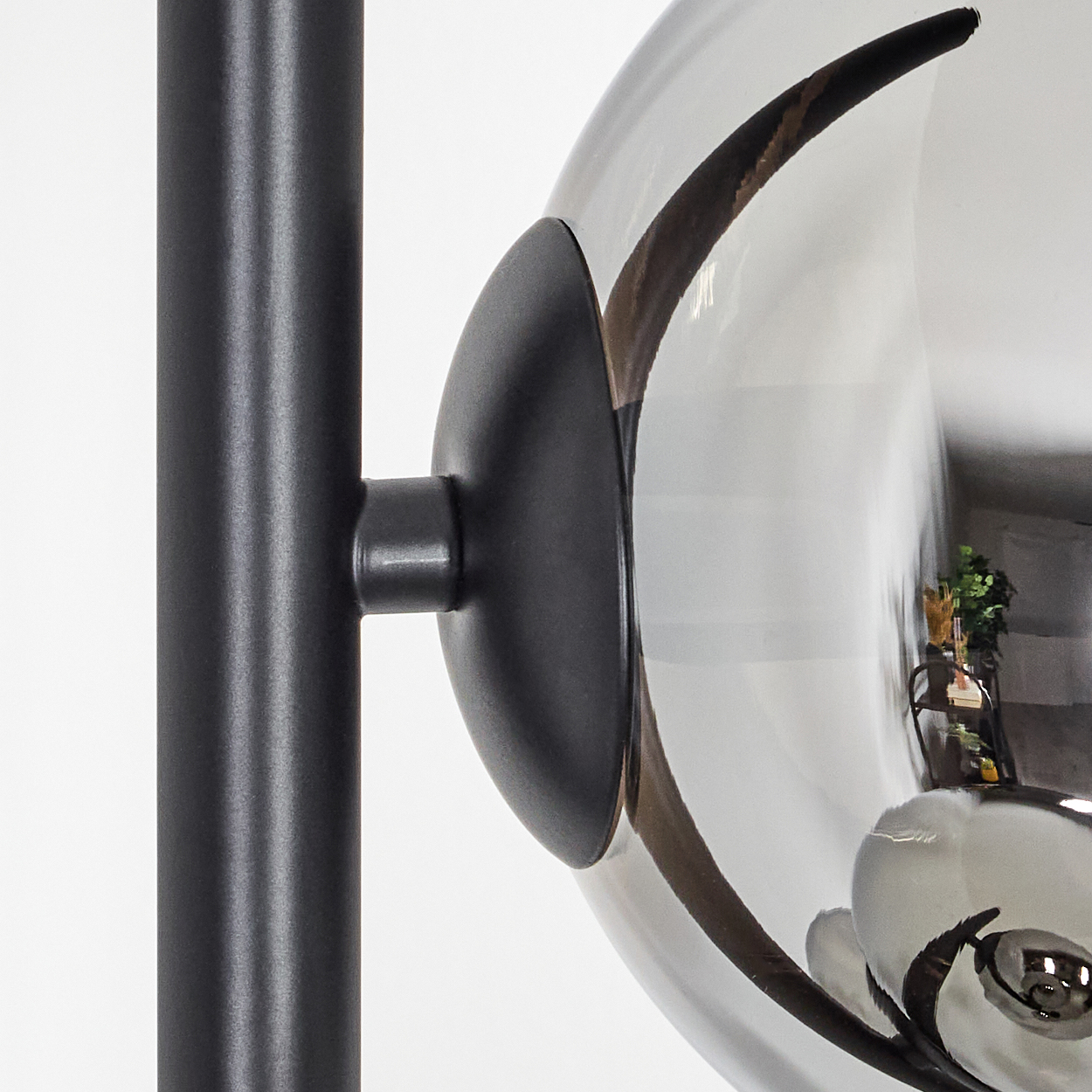 Nahaufnahme einer schwarzen Lampe. Eine graue Glaskugel spiegelt einen Raum mit grünen Pflanzen wider.