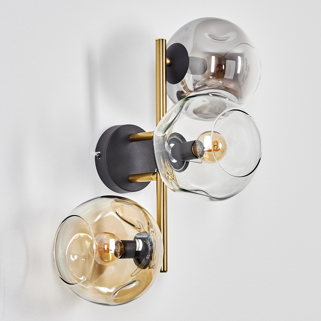 Eine moderne Wandleuchte mit drei Glaskugel-Schirmen, goldenen Akzenten und schwarzem Sockel, an einer weißen Wand befestigt.