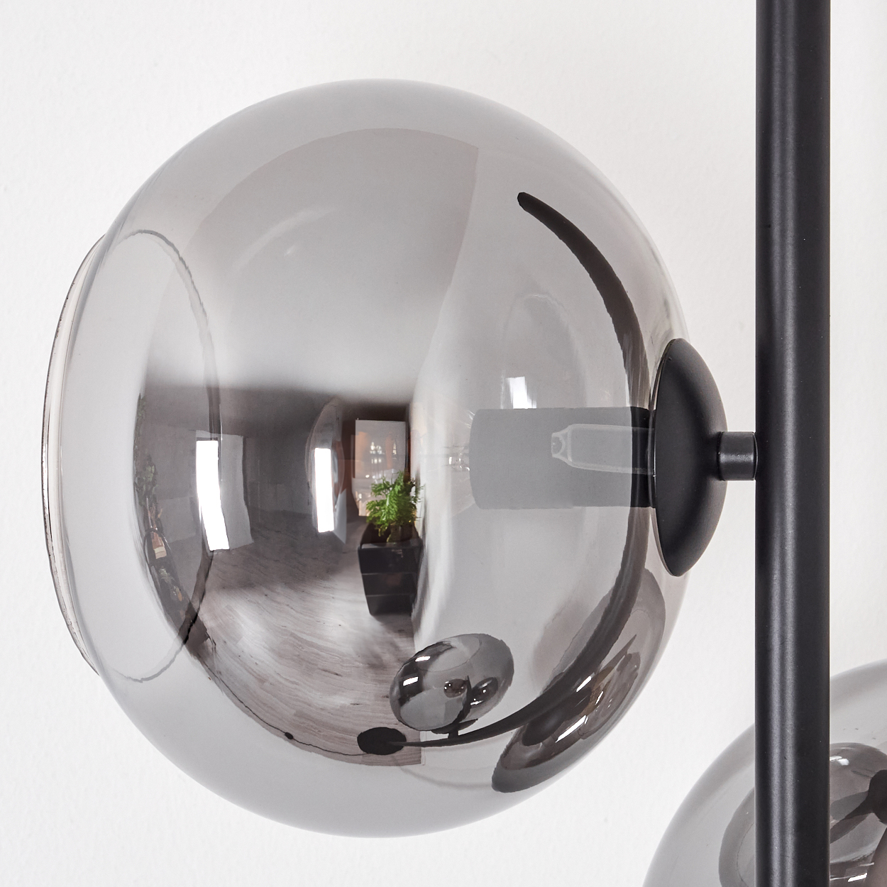 Nahaufnahme einer modernen Lampe mit einer transparenten, grauen Glaskugel. Die Kugel spiegelt einen Raum mit einer Pflanze.