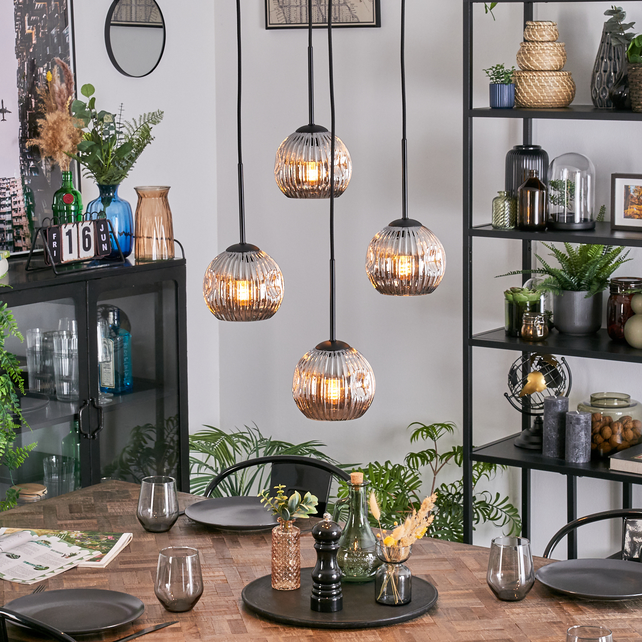 Ein Esszimmer mit Holztisch, Hängelampen und einem schwarzen Metallregal voller Dekoration.