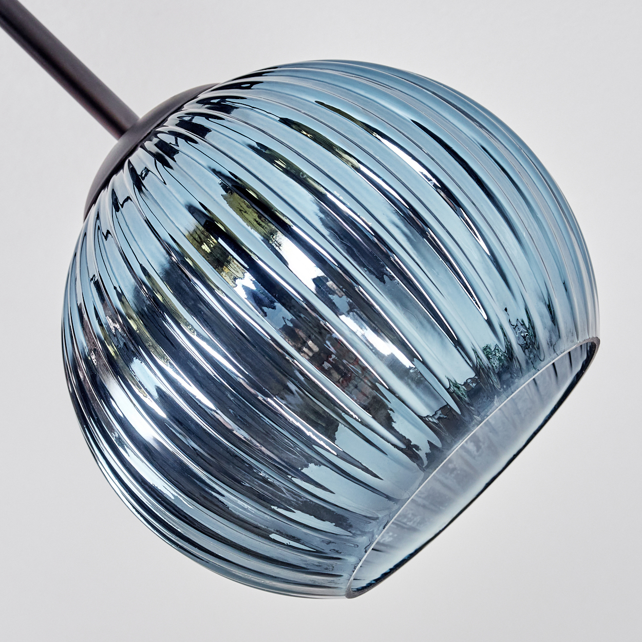 Nahaufnahme eines blauen Glaslampenschirms mit gerippter Textur, der an einer schwarzen Metallstange vor weißem Hintergrund hängt.