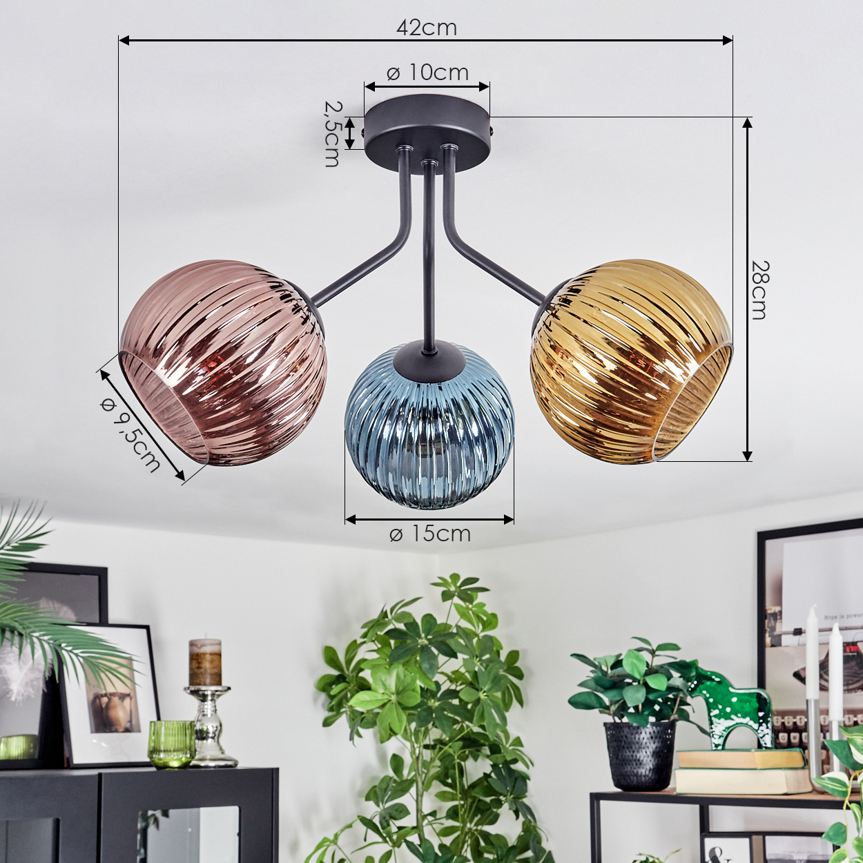 Eine Deckenleuchte mit drei Glasschirmen in Rosé, Blau und Gold. Maße sind angegeben. Pflanzen und Dekoration im Hintergrund.
