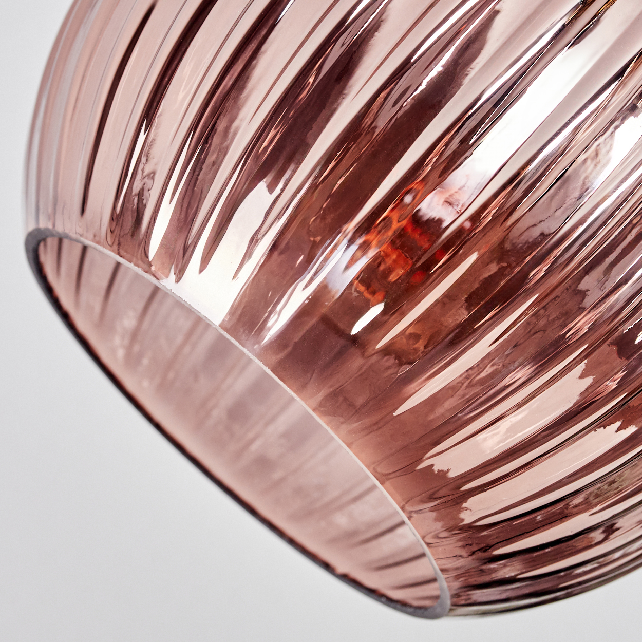Nahaufnahme eines rosafarbenen, gerippten Glasschirms. Das Licht spiegelt sich und zeigt Muster. Der Hintergrund ist weiß.