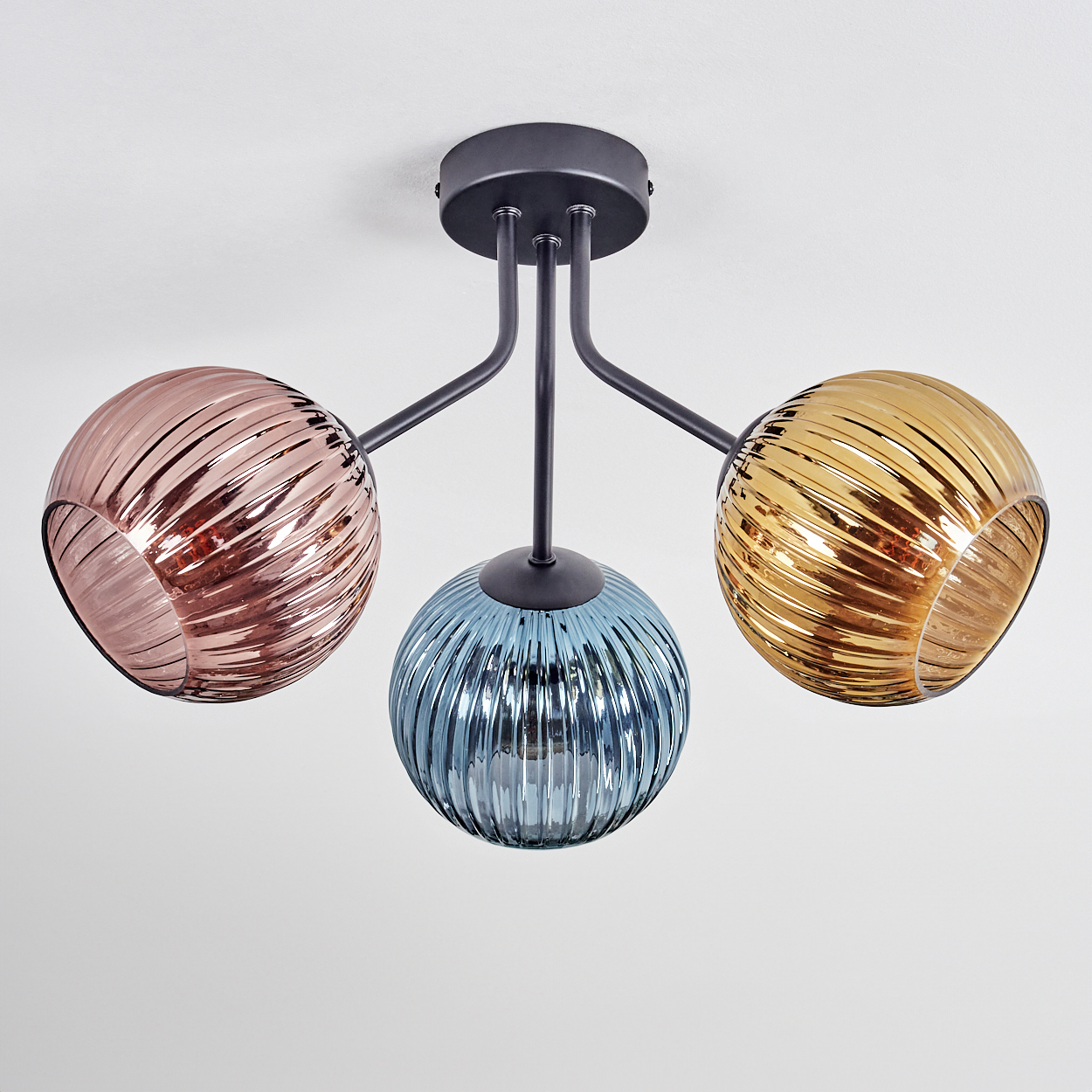 Moderne Deckenlampe mit drei kugelförmigen Schirmen in Rosa, Blau und Gold. Die Halterung ist schwarz, mit weißem Deckenhintergrund.