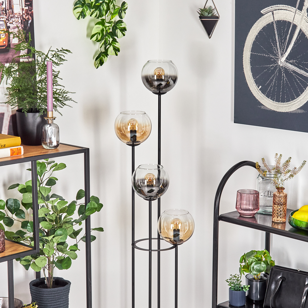 Ein modernes Interieur mit einer Stehlampe mit kugelförmigen Glasschirmen. Pflanzen und Dekoration befinden sich auf Regalen und Wänden.