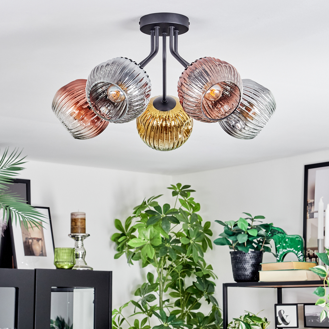Eine moderne Deckenlampe mit fünf Glasschirmen in Kupfer, Silber und Gold. Der Raum hat Pflanzen und gerahmte Bilder.