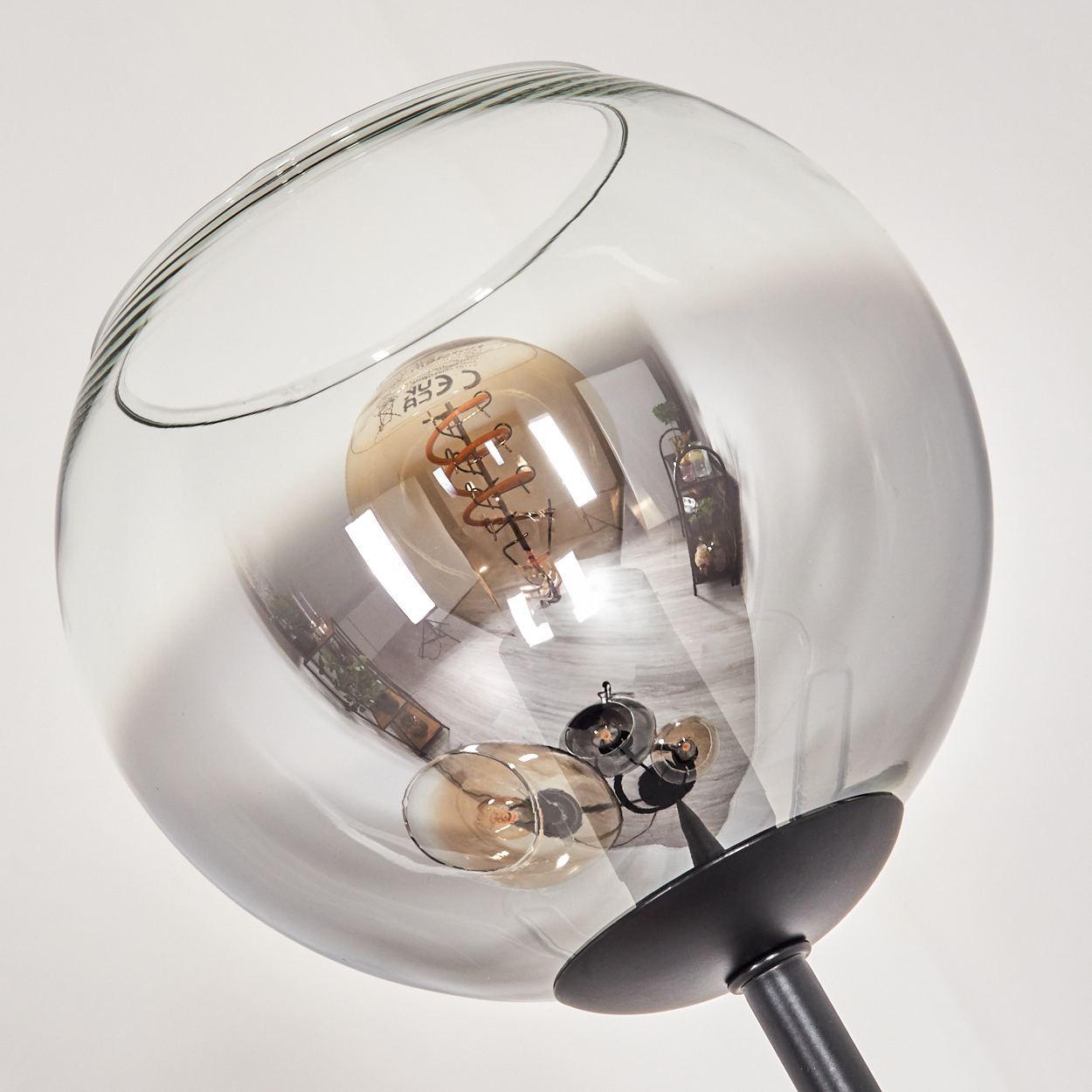 Nahaufnahme einer modernen Lampe. Sie hat einen klaren, kugelförmigen Glasschirm mit einer sichtbaren Glühbirne. Der Sockel ist schwarz.
