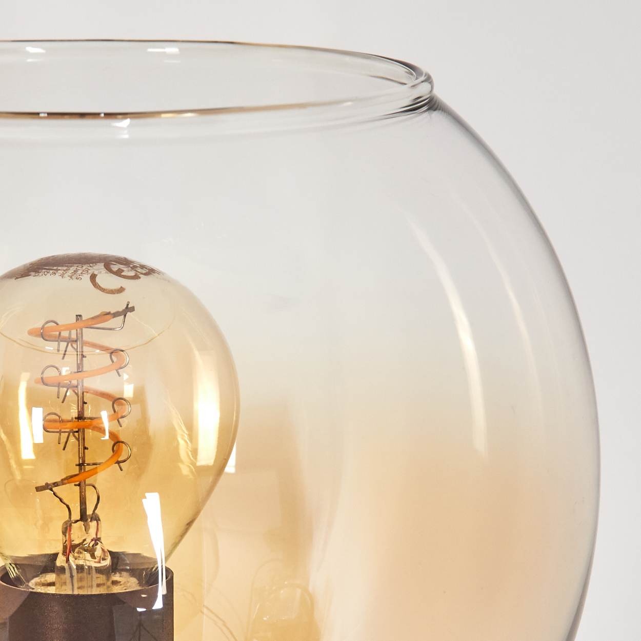 Nahaufnahme einer Glühbirne in einer Glaskugel. Die Glühbirne leuchtet, mit sichtbarem Wendel, das Glas ist klar.