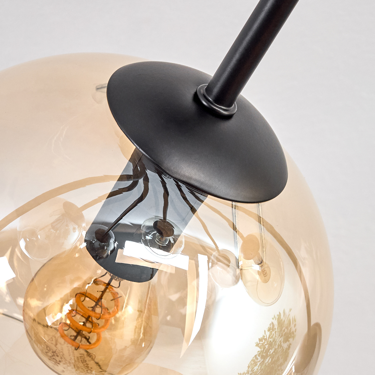 Nahaufnahme einer modernen Leuchte mit Glaskugel. Innen ist eine orangefarbene Glühbirne sichtbar. Schwarzes Metall stützt das Glas.