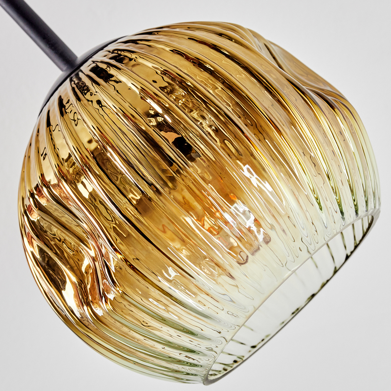 Nahaufnahme einer Glasleuchte mit goldenem Farbton und geriffelter Oberfläche, vor weißem Hintergrund.