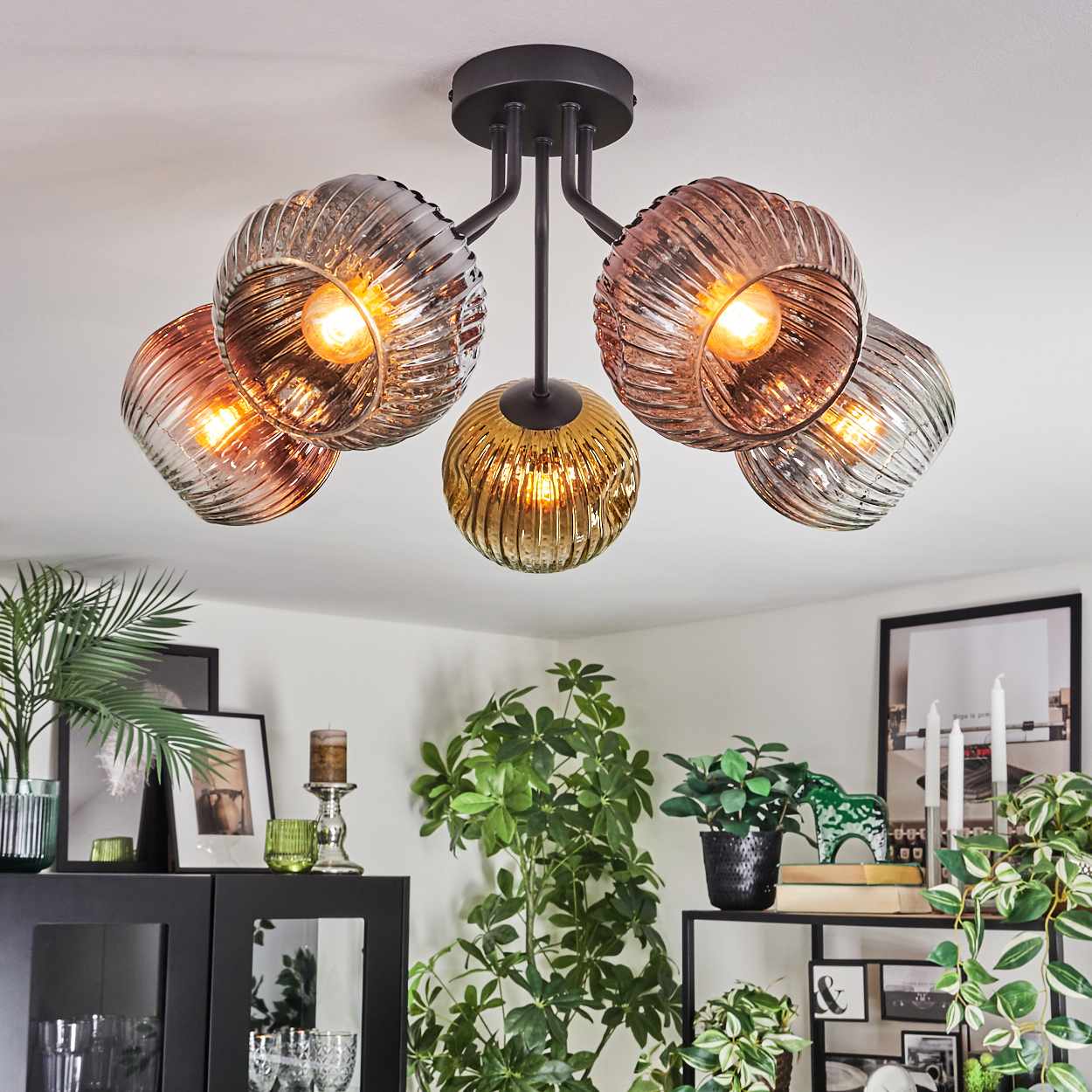 Eine moderne Deckenleuchte mit fünf Glasschirmen, die einen Raum mit Pflanzen und Dekoration beleuchtet. Die Decke ist weiß.