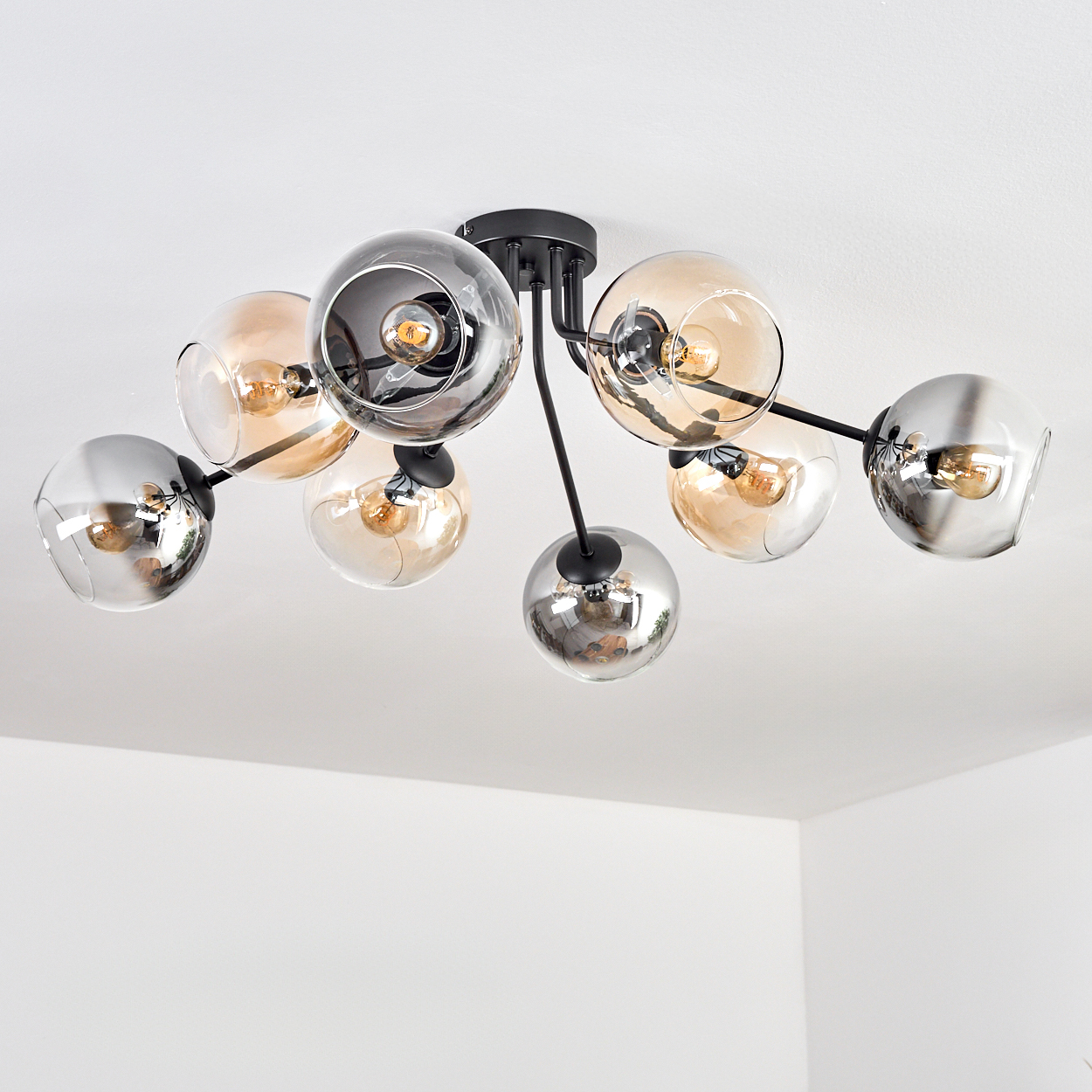 Eine moderne Deckenleuchte mit mehreren Glaskugelschirmen. Die Schirme sind in Silber- und Bernsteinfarben gehalten. Die Leuchte befindet sich an einer weißen Decke.
