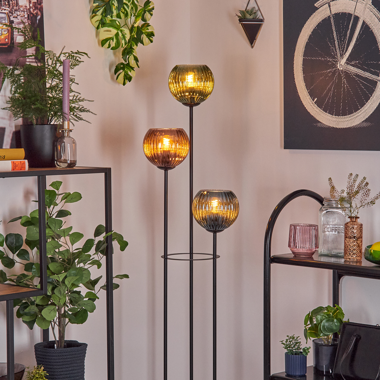 Ein modernes Wohnzimmer mit einer dreifachen Lampe, Pflanzen und Regalen mit Dekorationen, darunter ein Fahrradrad-Kunstwerk.