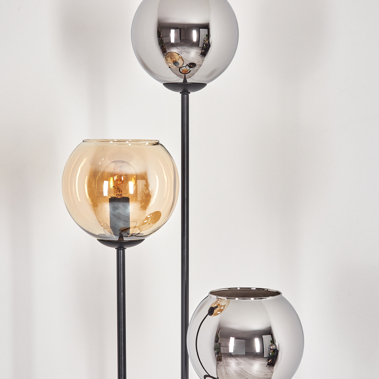 Eine moderne Stehlampe mit drei kugelförmigen Leuchten. Die obere und untere sind silberfarben, die mittlere bernsteinfarben. Der Hintergrund ist weiß.