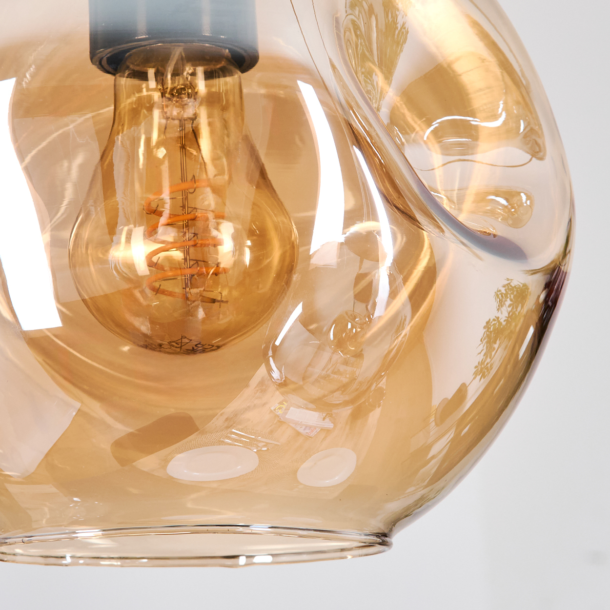 Nahaufnahme einer Glasleuchte mit einer warm getönten Glühbirne, die von einem transparenten, bernsteinfarbenen Glasschirm umgeben ist. Der Hintergrund ist weiß.