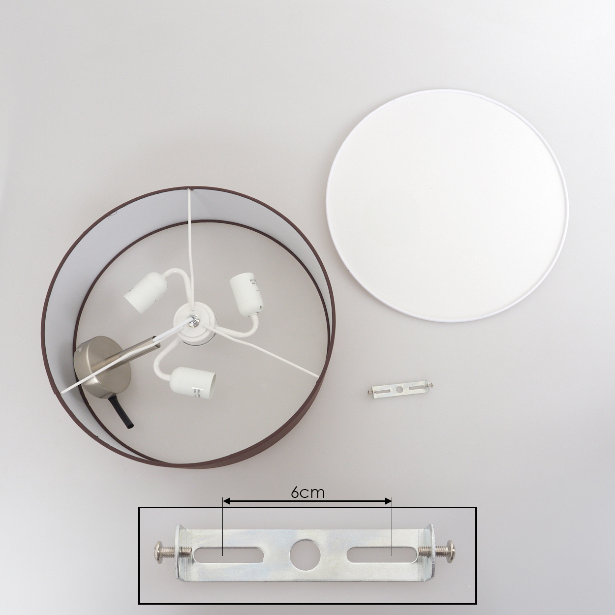 Draufsicht auf eine zerlegte Lampe. Sie umfasst einen Lampenschirm, eine weiße Deckenplatte, eine Halterung und eine Lampenfassung.