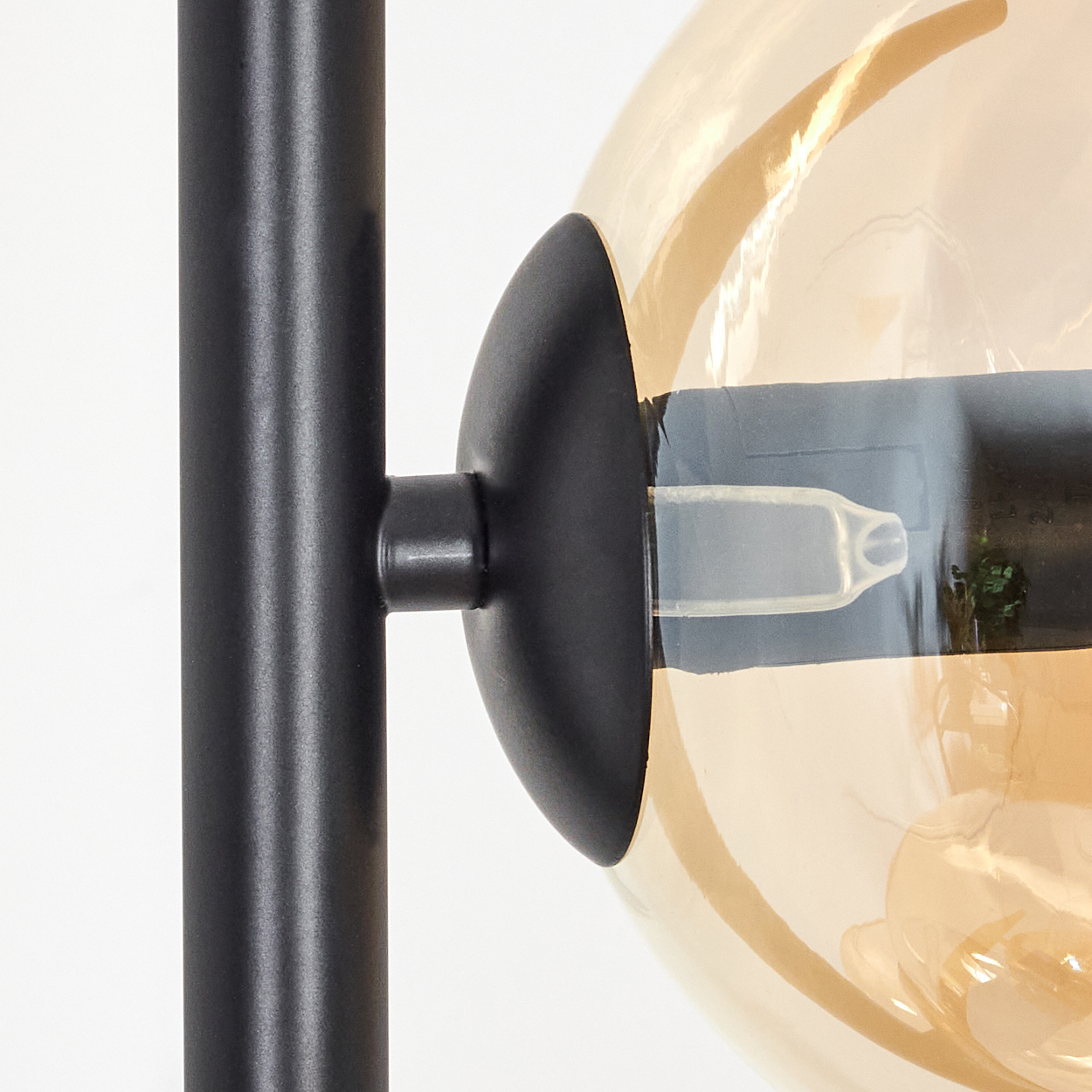 Nahaufnahme einer Lampe. Schwarzer Metallstiel und kugelförmiger Lampenschirm. Der Schirm ist bernsteinfarbenes Glas. Eine Glühbirne befindet sich im Schirm.