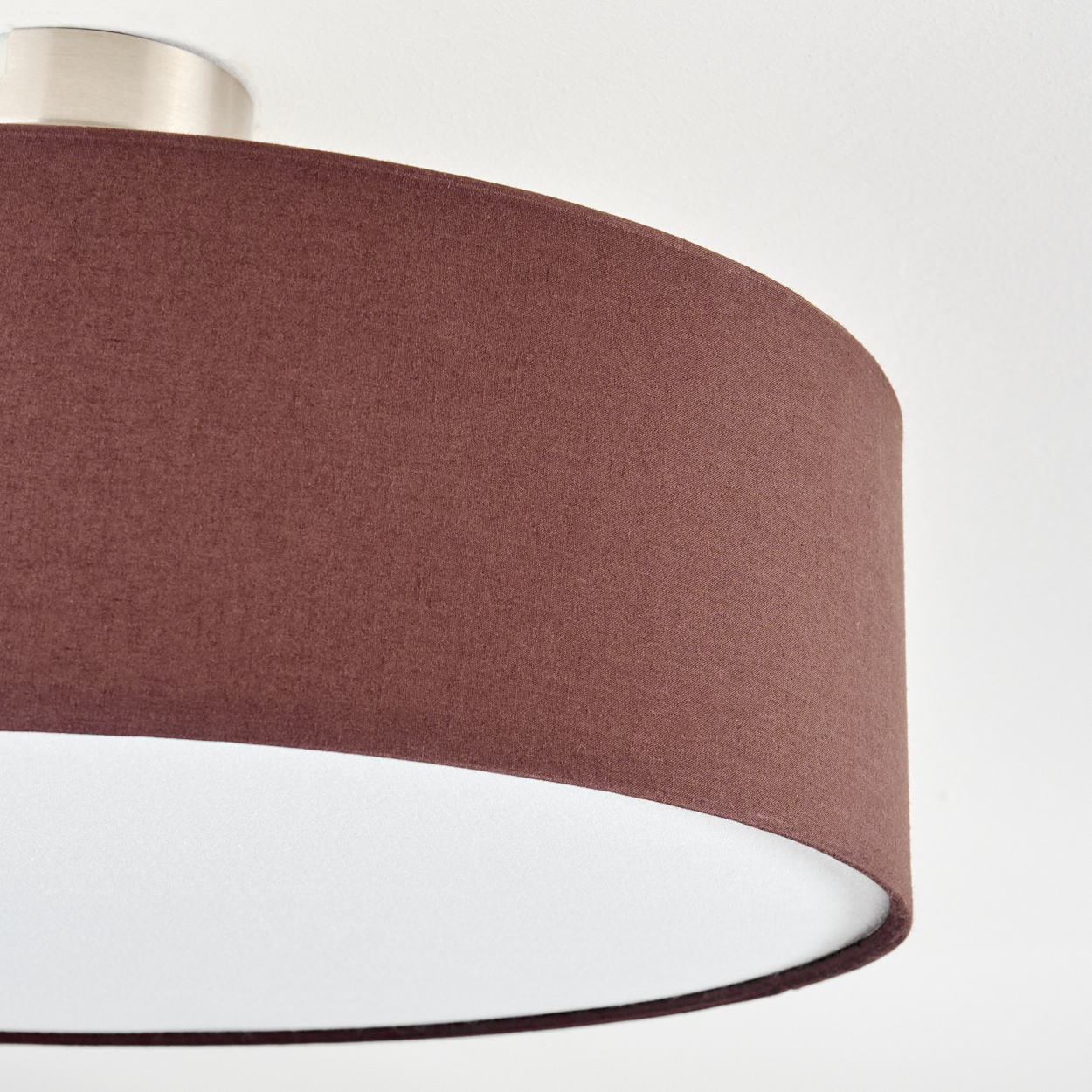 Nahaufnahme einer Deckenlampe. Sie hat einen braunen Stoffschirm mit weißem Innenraum. Die Deckenhalterung ist silber.