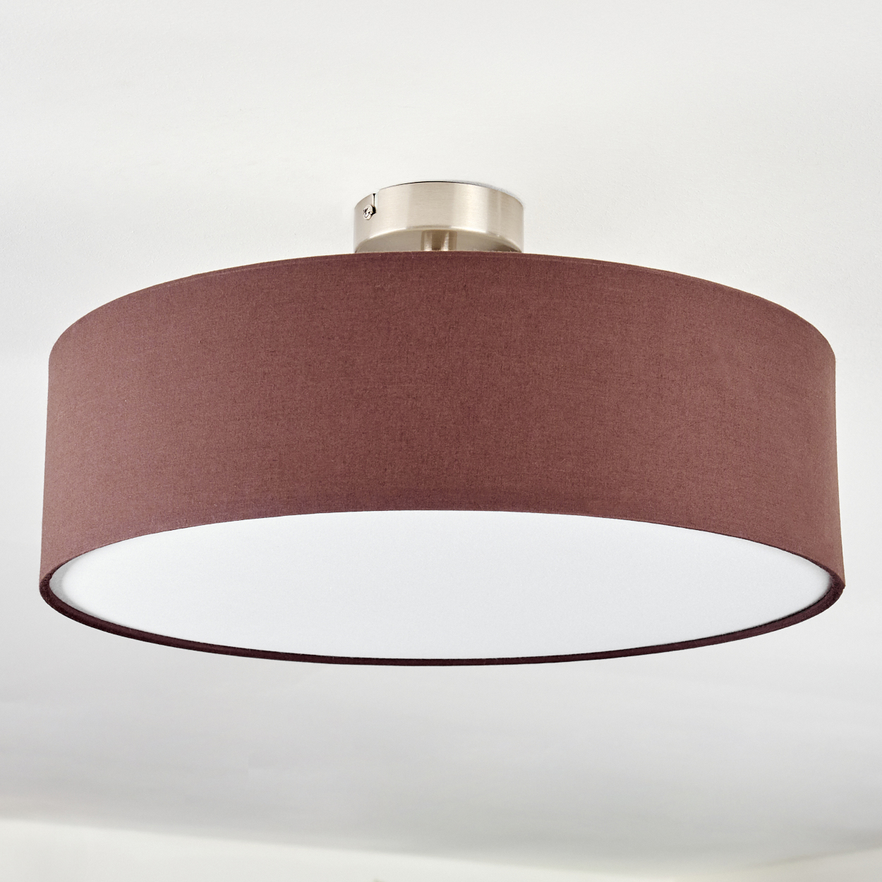 Eine Deckenleuchte. Sie hat einen maroonfarbenen Stoffschirm über einem weißen Innenraum. Die Leuchte ist mit einem silbernen Sockel an einer weißen Decke befestigt.