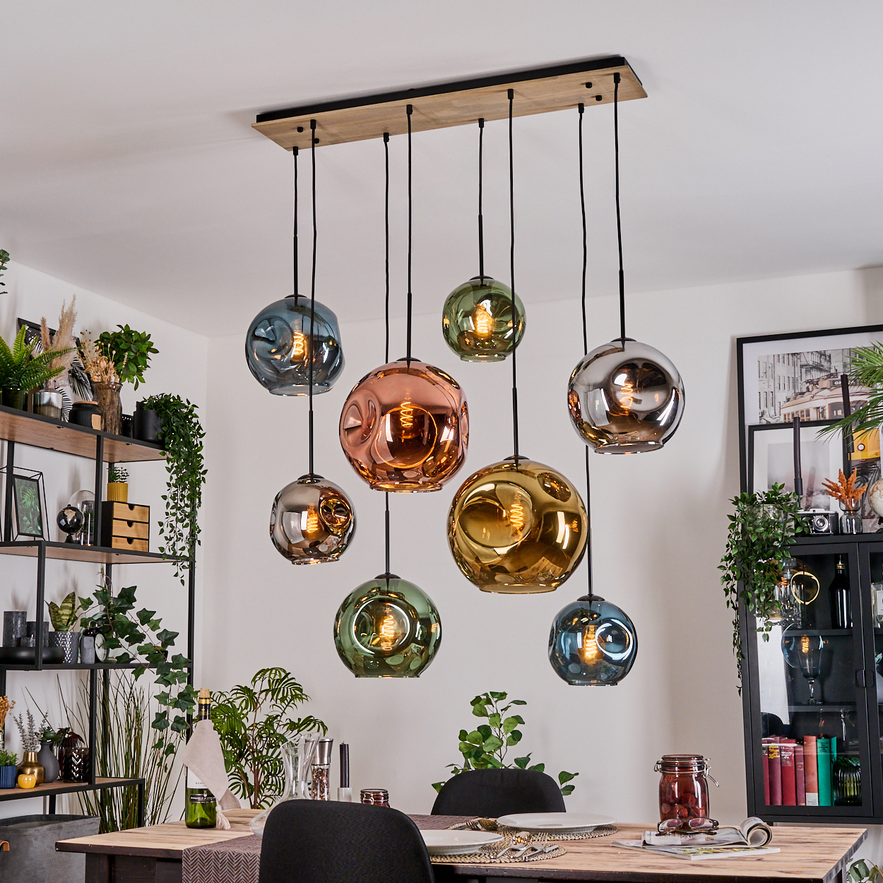 Neun bunte Glaskugel-Pendelleuchten hängen über einem Esstisch. Der Raum hat ein modernes Design mit Pflanzen und Dekor.