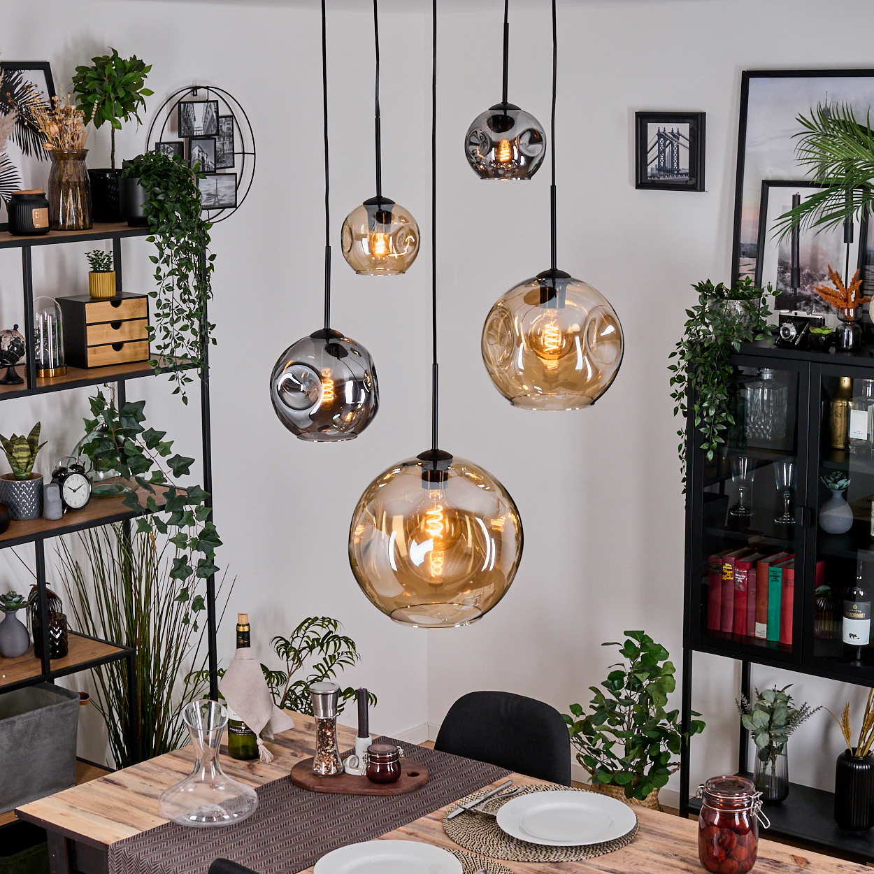 Esszimmer mit Hängelampen, Holztisch, gedeckt für das Abendessen, dekorativen Regalen und Pflanzen.