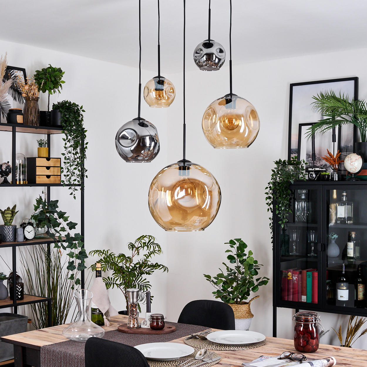 Esszimmer mit Pendelleuchten, Tisch gedeckt. Pflanzen und Dekoration vorhanden. Warme Beleuchtung und moderne Ästhetik.