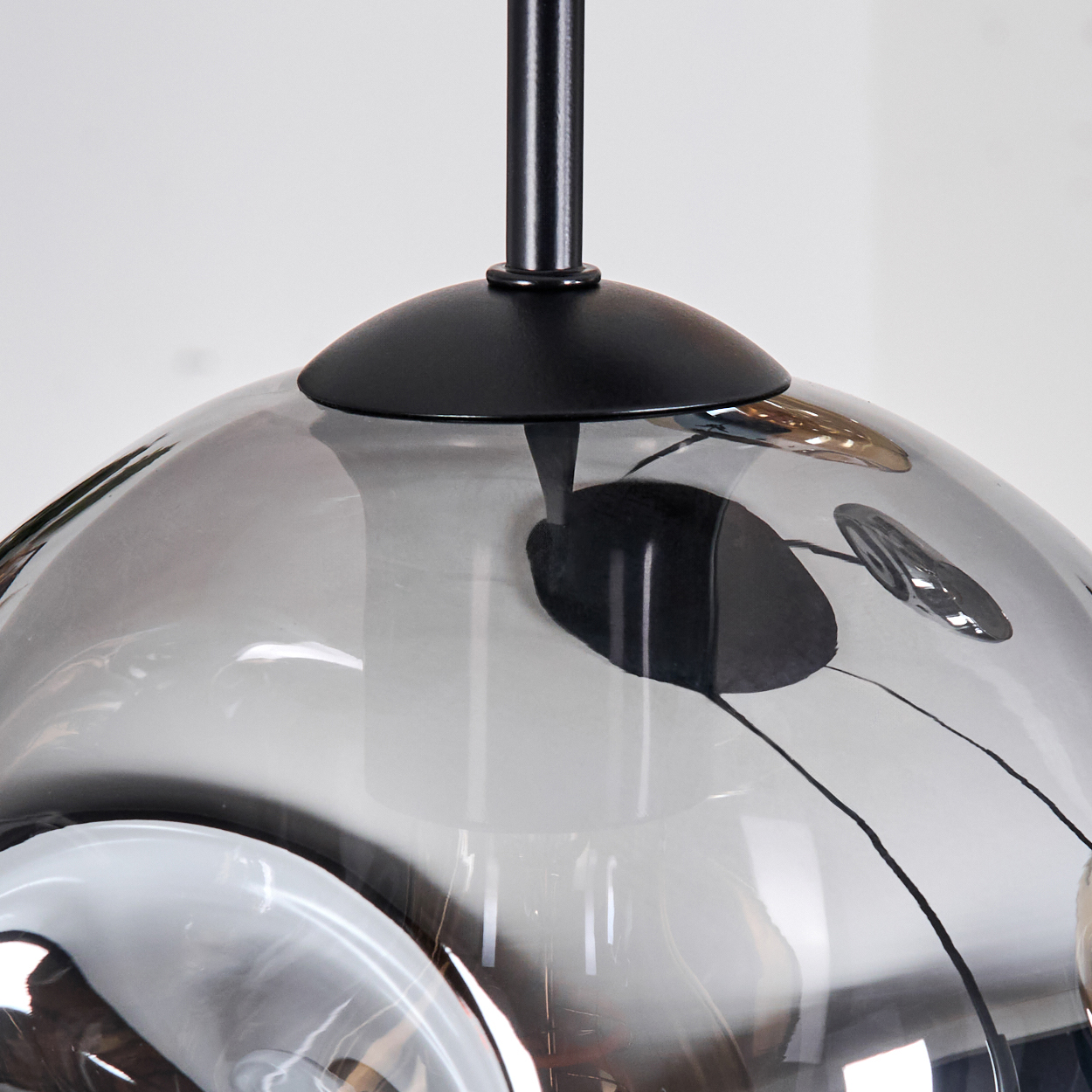 Nahaufnahme einer modernen Pendelleuchte aus Rauchglas mit schwarzen Metallakzenten. Die Leuchte hat eine einzigartige, geschwungene Form und hängt an einer schwarzen Stange.
