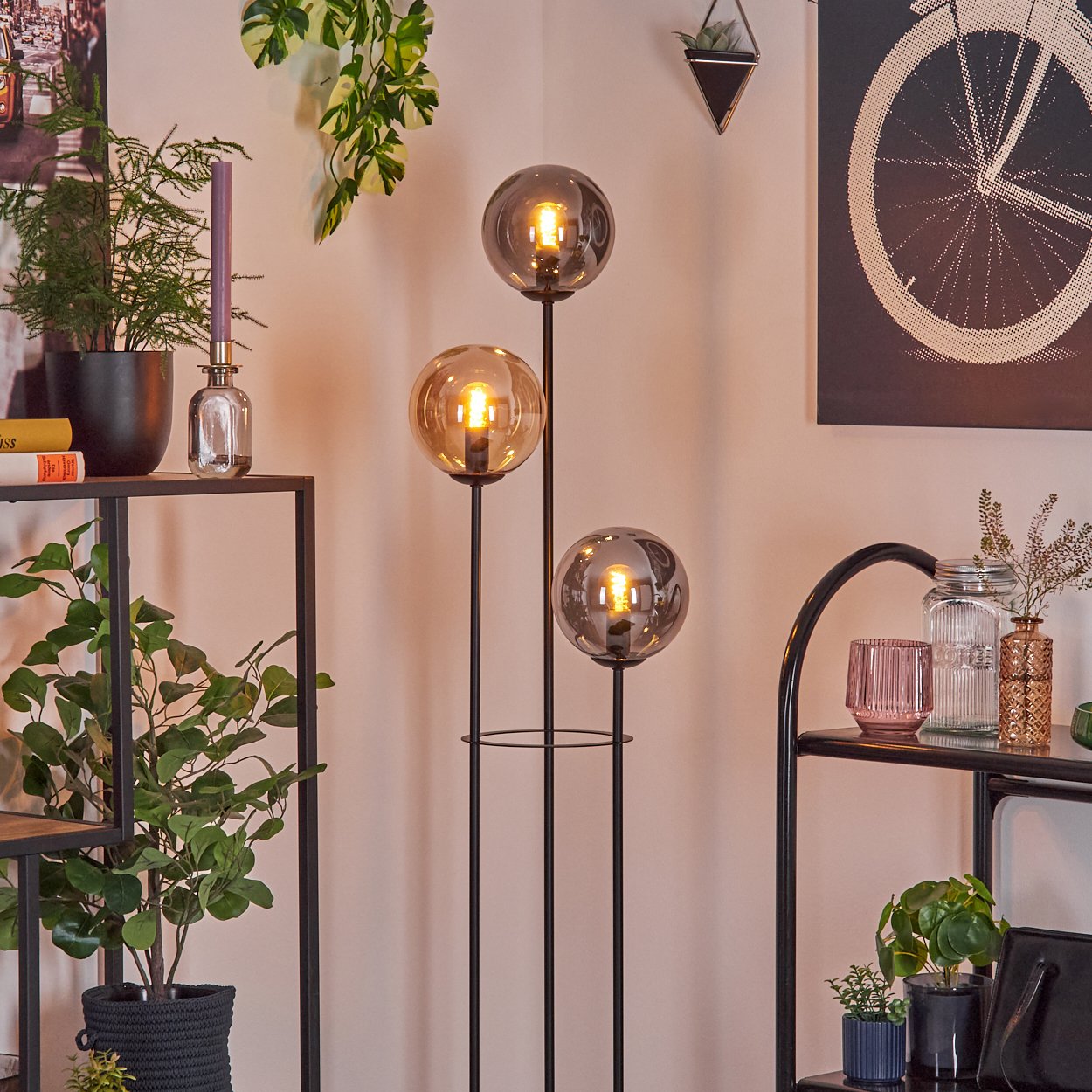 Eine moderne Zimmerecke mit einer Stehlampe mit drei Glaskugeln, Pflanzen und Regalen mit Dekorationsartikeln.