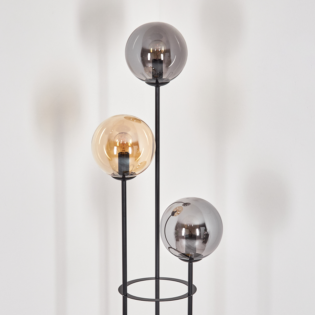Moderne Stehlampe mit drei kugelförmigen Schirmen. Zwei sind grau, einer bernsteinfarben. Schwarze Stiele und ein kreisförmiger Sockel.