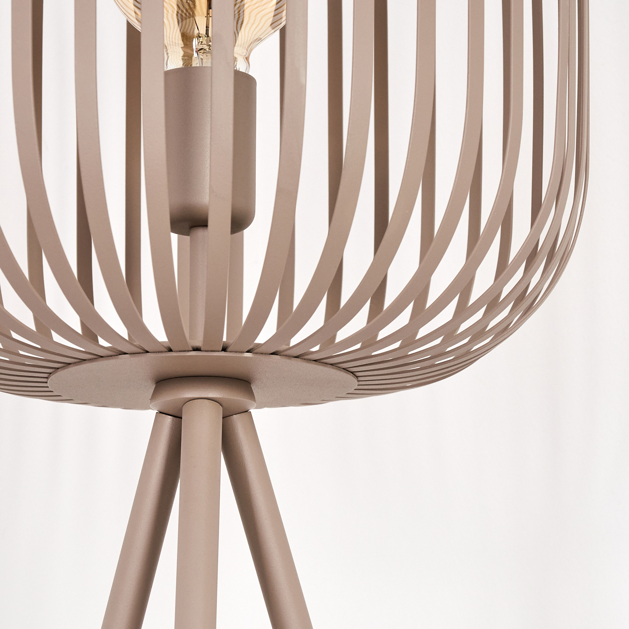 Nahaufnahme einer braunen Lampe mit käfigartigem Lampenschirm und sichtbarer Glühbirne, getragen von drei Beinen, vor weißem Hintergrund.