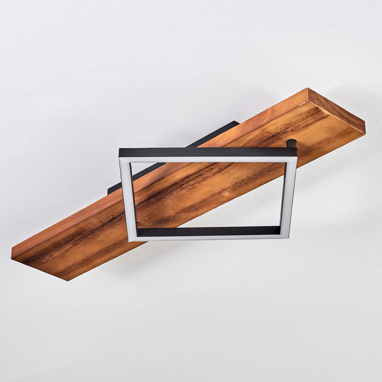 Eine moderne Deckenleuchte mit Holzbohle und quadratischer Leuchte mit weißem Rahmen. Der Hintergrund ist eine weiße Wand.