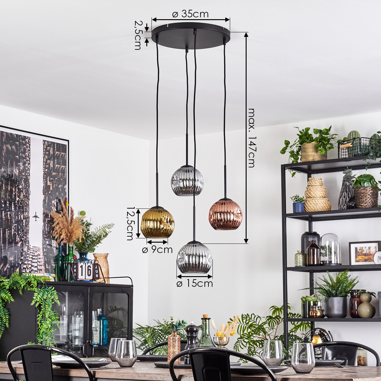 Ein Esszimmer mit einer schwarzen Pendelleuchte mit vier kugelförmigen Lampenschirmen, einem Tisch mit Gläsern und Pflanzen.