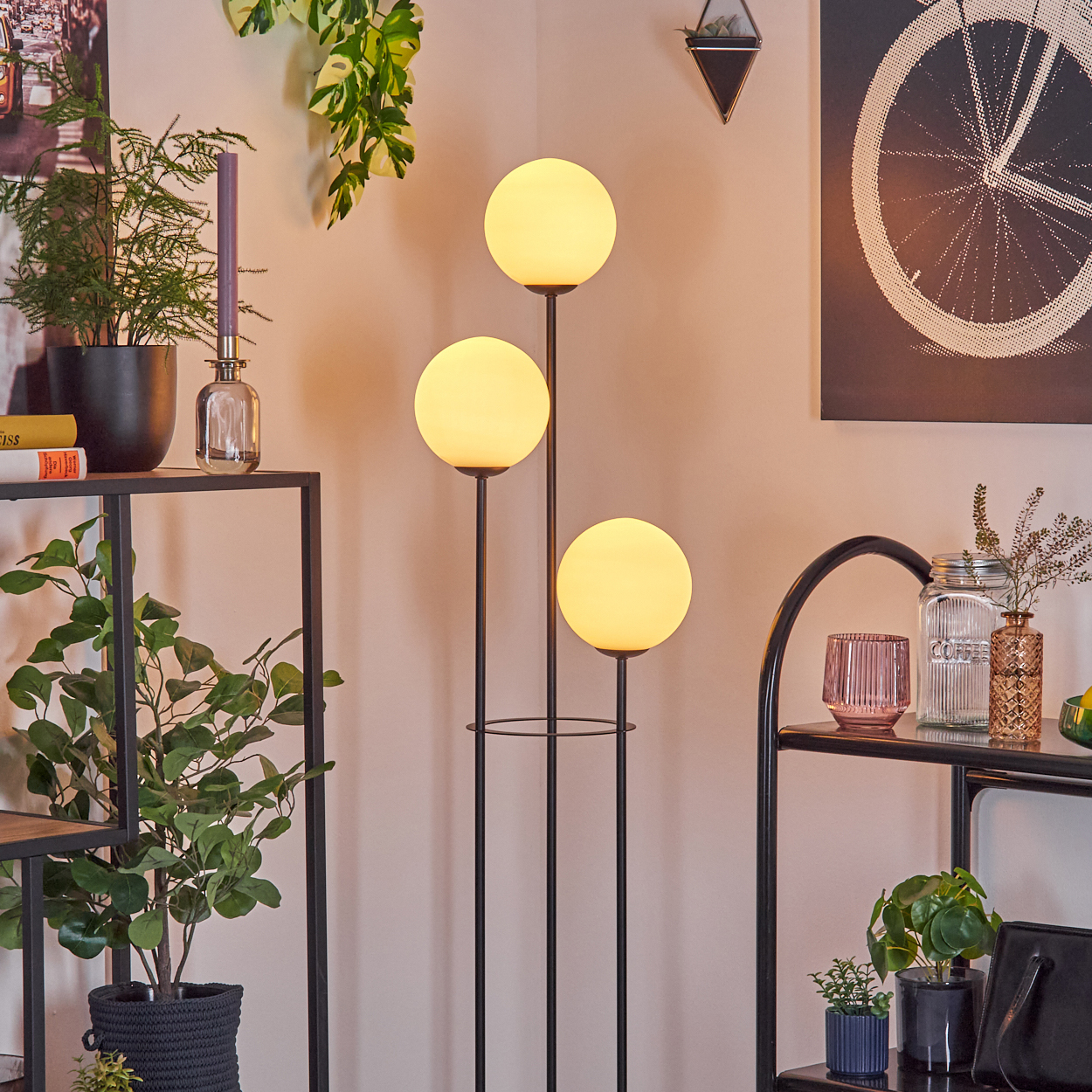 Raumecke mit Stehlampe mit runden Lichtern. Regale mit Pflanzen, Kerze und Deko. Fahrradrad-Kunst an der Wand.