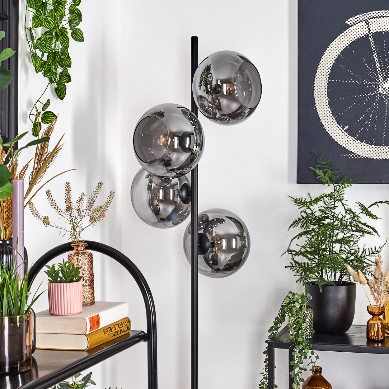 Ein modernes Interieur mit einer schwarzen Stehlampe mit Glaskugeln, Pflanzen und einem schwarzen Regal. Kunstwerk eines Fahrradrads an der Wand.